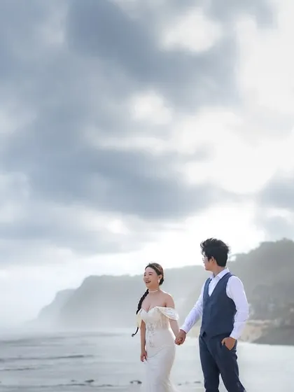 A candid moment of laughter on a beautiful Bali beach. The overcast sky creates a soft, even light that is perfect for capturing natural emotions and the stunning coastal scenery.
