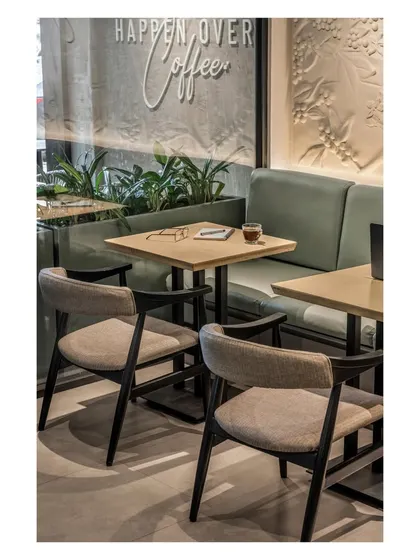 The seating arrangement combines soft textures, earthy tones, and a thoughtful layout to ensure the setting is as inviting as the coffee it serves. The brand's tagline is visible on the glass, reinforcing the atmosphere.