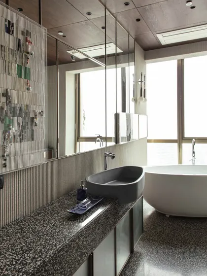 The daughter's bathroom is a chic sanctuary, featuring a custom wash basin by Gomaads, terrazzo flooring, and delicate paper art by Ashoka Acharya. The space is a blend of style and function, designed for relaxation.