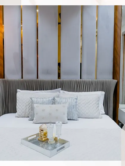This bedroom is designed to be a calming escape. The headboard features pleated grey fabric with vertical gold strips, creating a sophisticated and modern look.