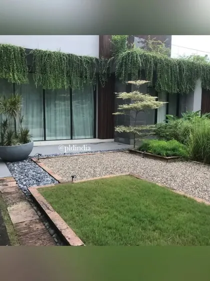 A Zen-inspired courtyard featuring a mix of grass, gravel, and stone, set against a building with a dramatic vertical garden. The design creates a sense of calm and order through its clean lines and natural materials.