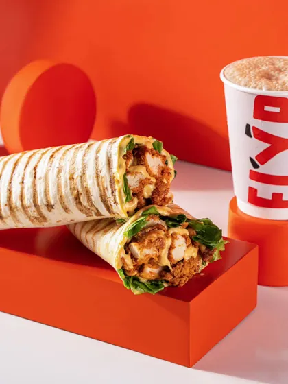 A chicken wrap and coffee from Flyp, styled with bold orange props. This shows a complete meal option, appealing to customers looking for a quick and tasty combo.