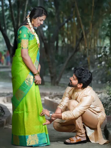 A sweet and traditional pre-wedding moment, where the groom-to-be helps his fiancée with her footwear. This candid-style shot captures a gesture of care and affection between the couple.