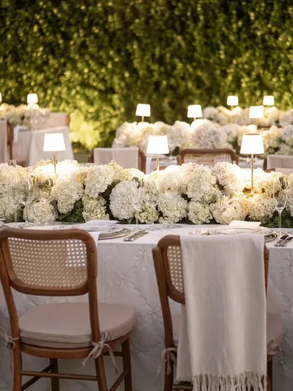 A close-up shot of the elegant dinner setting, with a wall of green foliage providing a lush, natural backdrop to the crisp white tables.