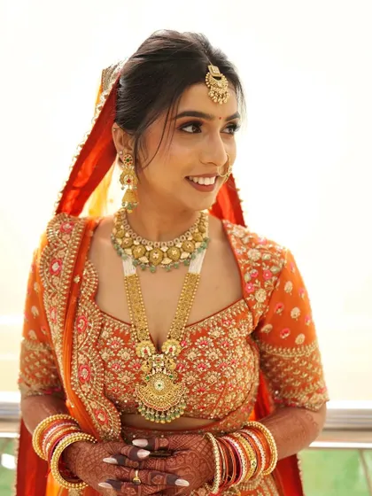 A radiant bride in a beautiful orange lehenga, her makeup features warm tones and a glowing finish.