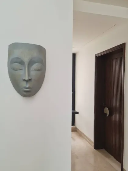 A serene sculptural mask mounted on a clean white wall, adding a touch of contemplative art to a quiet corridor. This snippet from a recently completed residence showcases our love for integrating art into our designs.