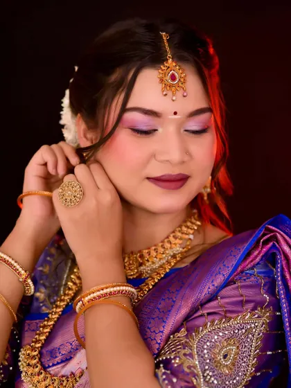 A South Indian bride getting ready. The focus is on traditional gold jewelry and a radiant makeup look with a pop of color on the eyes and lips.