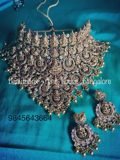 A wide temple jewellery choker with intricate Lakshmi carvings and pearl drops. This is a standout piece available for rent.