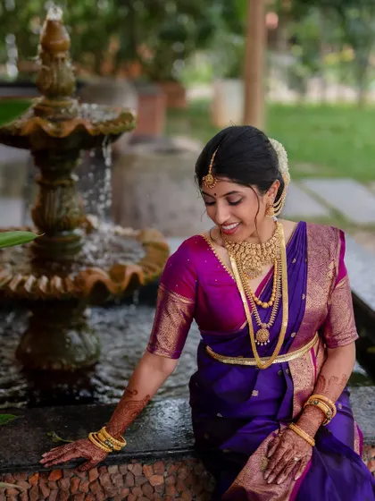 A moment of quiet reflection for the bride. Her vibrant purple and pink saree and traditional gold jewelry are beautifully highlighted in this classic portrait.