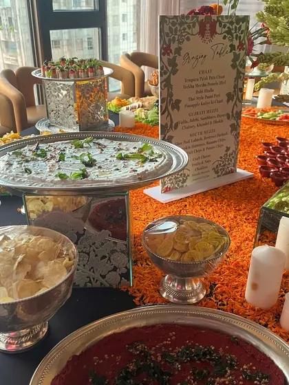 A festive grazing table featuring a variety of dips and chips, including beetroot hummus and a yogurt-based dip. The setup is decorated with marigold petals and candles, perfect for a Diwali or wedding celebration.