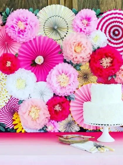 A cake table should be a centerpiece of any celebration. For this party, I created a vibrant and joyful backdrop using a dense arrangement of colorful paper fans and paper flowers in shades of pink, white, and yellow, making the cake presentation extra special.