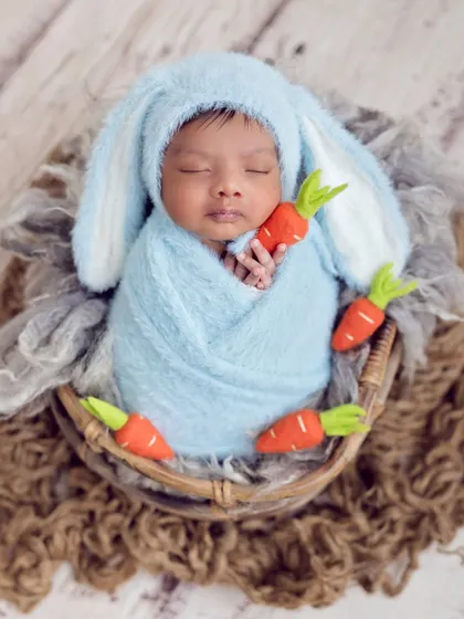 A sweet little bunny snuggled in a basket. The fluffy blue bunny hat and tiny carrots make for an incredibly cute and memorable portrait.
