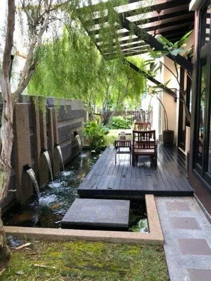A modern water feature with multiple spouts creating gentle streams into a pond. This design, set against a textured stone wall and surrounded by lush greenery, adds a sophisticated and calming element to the landscape.