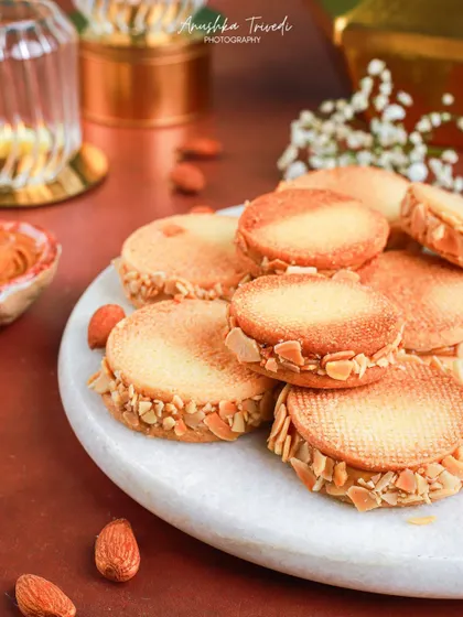 A platter of almond sandwich cookies, neatly arranged on a marble plate for a clean and elegant presentation.