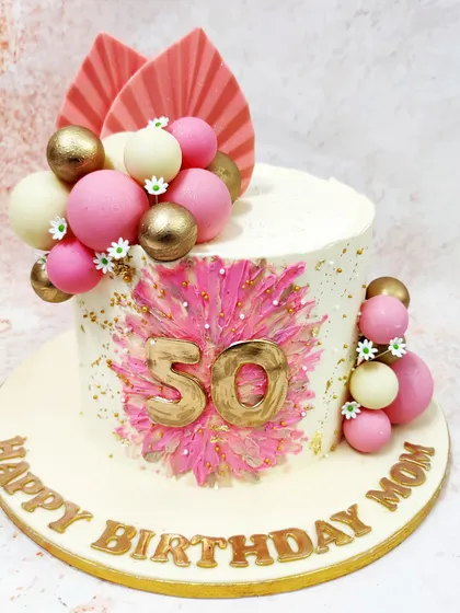 We celebrate a 50th birthday with this vibrant and modern pink boho cake. A bold pink starburst design with a gold "50" is the centerpiece, complemented by pink, white, and gold spheres and dried palm leaves for a chic, bohemian look.