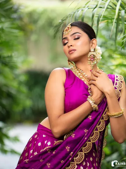 The rich purple of this lehenga stands out beautifully against a natural green backdrop. This image showcases the outfit's scalloped dupatta border and intricate gold detailing.