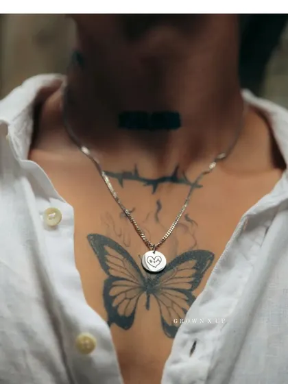 A silver-toned round pendant engraved with a simple, hand-drawn style heart. This piece, worn against a butterfly tattoo, shows how my jewelry can complement your personal story and style.