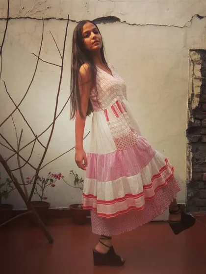 A model wearing a unique tiered patchwork dress in shades of pink and white. This bohemian-inspired design combines different prints and textures for a playful and artistic look.