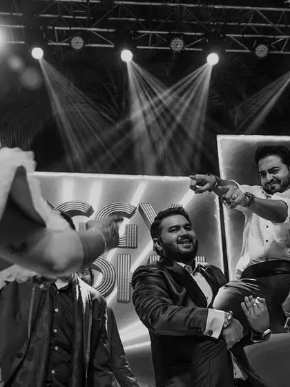 A black and white shot of the Sangeet party, with the groom being lifted on friends' shoulders as the bride dances.