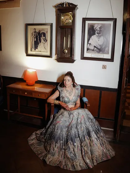 Another elegant portrait of the bride seated, showcasing her beautiful lehenga and the classic decor of the venue.