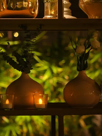 Two terracotta vases with simple greenery, flanked by small candles. The backdrop of lush, out-of-focus greenery creates a beautiful, layered effect.