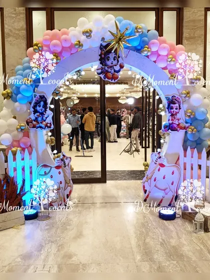 A divine entrance for the Krishna-themed party, featuring a circular arch with Krishna cutouts, peacock feathers, and a white picket fence.