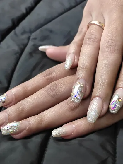 A dazzling set of long, square-tipped extensions with a glitter base, enhanced with large iridescent crystals and smaller gold studs.