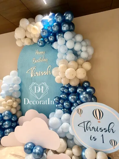 A personalized sign announces "Thrissh is 1" amidst a sea of blue and white balloons and cloud props.