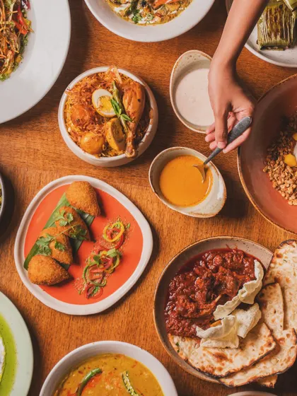 Another angle of a shared Indian feast, this time with a spoon dipping into a sauce. These small actions create a dynamic and engaging scene that tells the story of a delicious meal in progress.