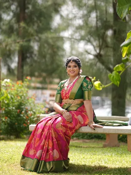 Seated in a garden, Devika's pink saree looks vibrant and beautiful against the natural greenery.