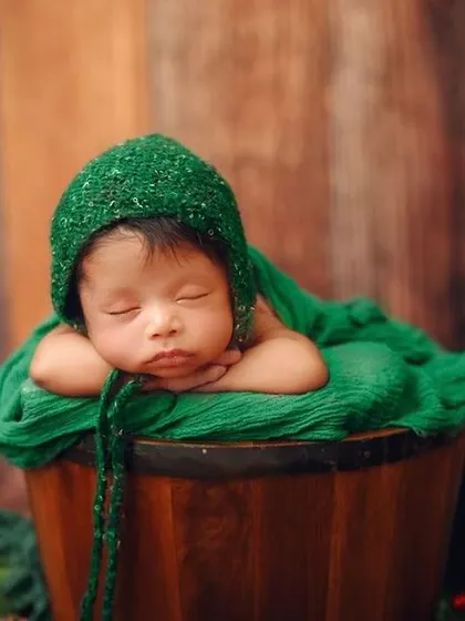 This classic 'potato sack' pose is a favorite for showing how curled up and tiny newborns are. The rich green wrap and rustic wooden backdrop create a beautiful, earthy portrait.