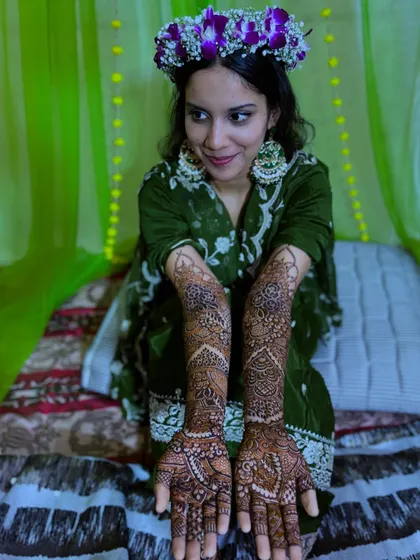 A full-length shot of the bride sitting, showcasing her complete bridal henna on both hands.