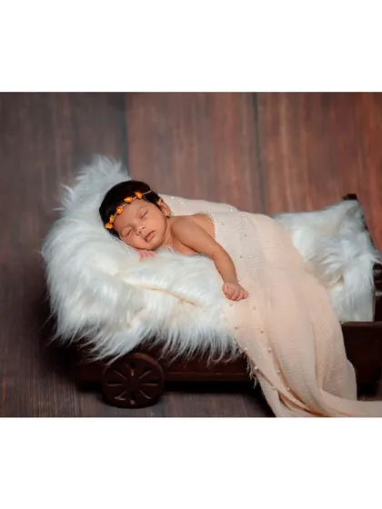 A full shot of a newborn sleeping on a tiny wooden cart prop.