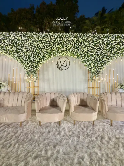 A close-up of the elegant seating on the all-white stage, with a custom monogram and a cascading canopy of white flowers creating a dreamy, romantic setting.