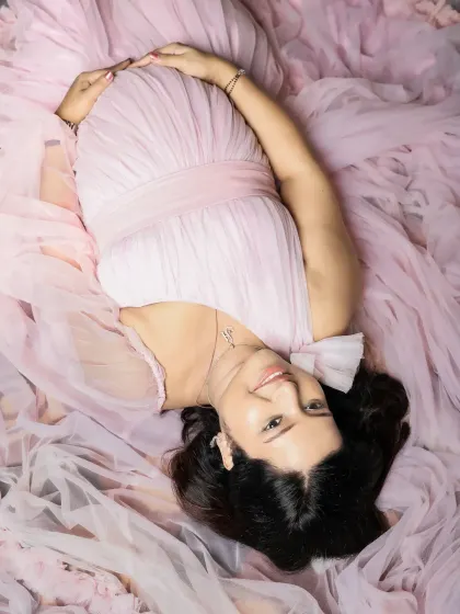 A unique perspective capturing the pregnancy glow. This overhead shot shows the mom-to-be lying on a bed of soft pink tulle, looking up with a gentle smile.