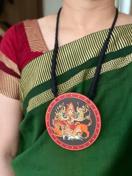 A powerful depiction of Maa Durga in her warrior form, hand-painted on a large wooden pendant. Wearing this piece feels like carrying a symbol of strength and protection.
