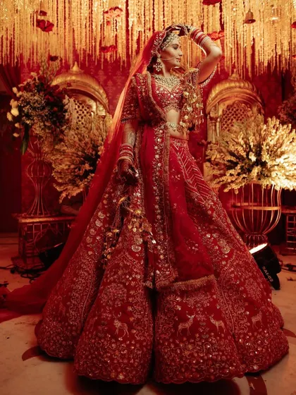 The bride, in her magnificent red lehenga, is the centerpiece of the royal decor. The golden and floral backdrop perfectly complements her regal attire.