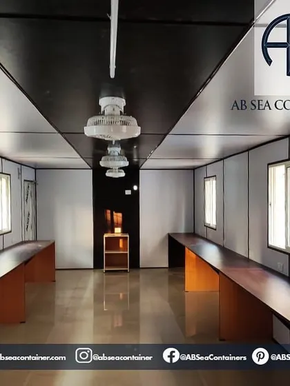 This image shows the clean and functional interior of a container office. It is equipped with long desks, lighting, and fans, creating a productive workspace for any remote site.