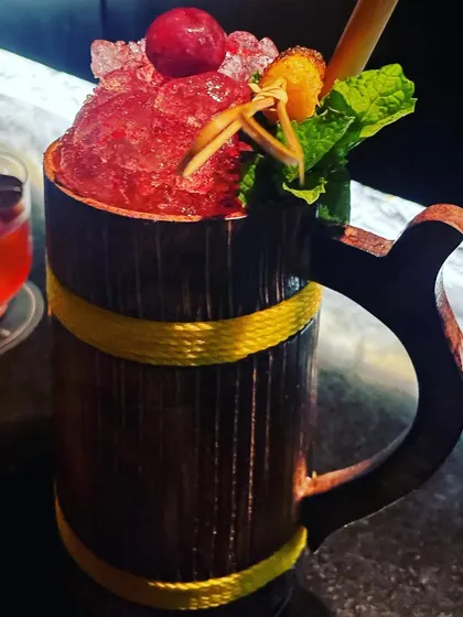 A fun and fruity cocktail served in a rustic wooden mug. The crushed ice, fresh mint, and cherry garnish make it a perfect choice for a tropical-themed party.