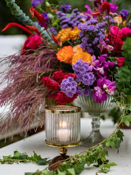A detailed shot of one of the colorful floral arrangements on a side table, illuminated by a candle. The mix of purples, reds, and oranges creates a rich and beautiful composition.