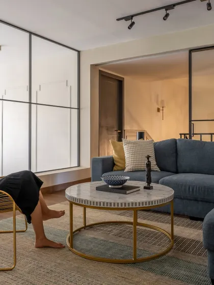 The family room, tucked away on the upper level, is a calm, laid-back space for the family to gather. A comfortable blue sectional sofa and a marble-topped coffee table create a relaxed and modern vibe.