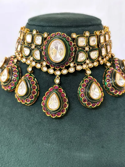 A close-up of a bridal choker with large Kundan stones and green and red Meenakari enamel work. This statement piece is available for rent for your special day.