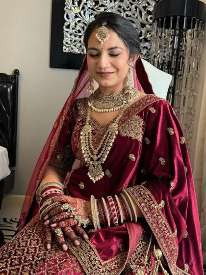 A stunning North Indian bride in a traditional red velvet lehenga. The makeup is classic and timeless, with a focus on flawless skin and defined features.