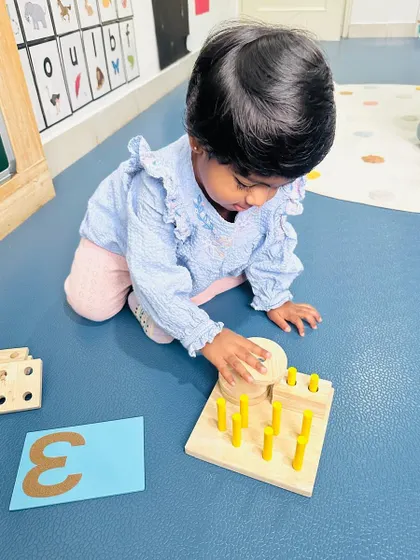 A toddler works with a wooden peg puzzle, matching the number of pegs to the corresponding numeral, a classic Montessori-inspired numeracy activity.