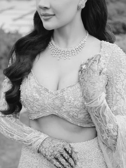 A soft and romantic black and white close-up of the bride, highlighting the delicate embroidery of her blouse and the intricate henna on her hands.