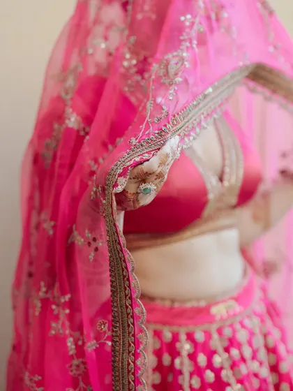A detail shot of Akanksha's pink lehenga, with the veil gently obscuring the frame. The focus on the texture and color is artistic and beautiful.