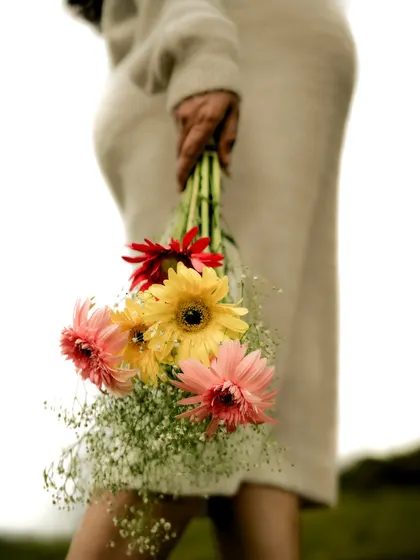 A close-up, artistic shot focusing on the colorful bouquet of flowers held by the mom-to-be, with her baby bump visible in the background.