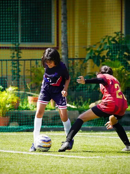 A young player shows great determination as she shields the ball from a defender in a closely contested match.