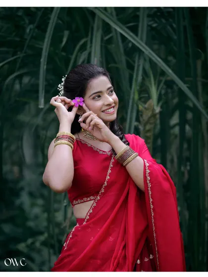 A close-up of the bride-to-be's happy smile as she adorns her hair with a flower, set against a natural green background.