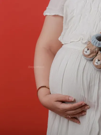 A close-up focusing on the baby bump, with the mom-to-be holding a pair of adorable knitted baby booties.